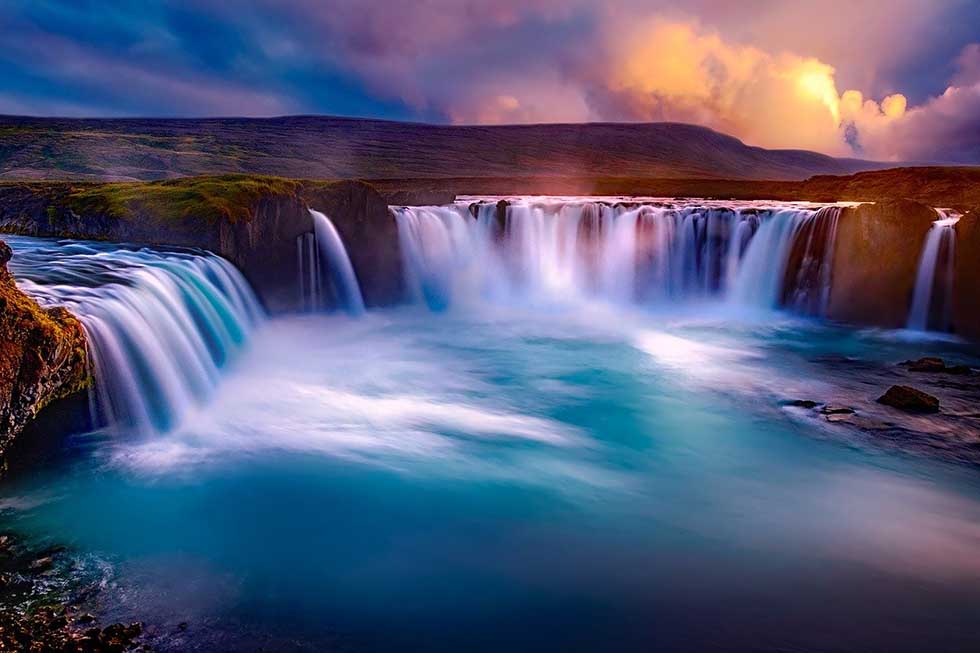 A large waterfall bordered by rocky cliffs under a sunset sky.