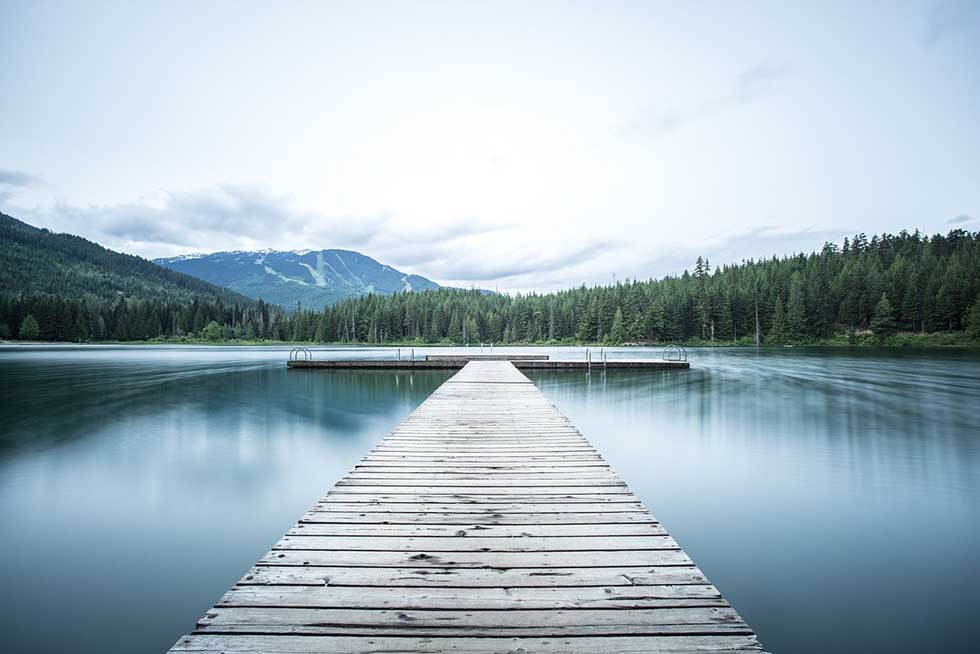 wooden pier in middle of lake surrounded by trees